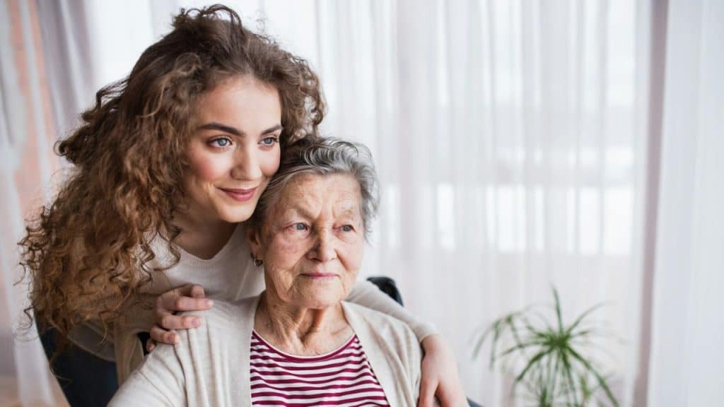 A younger woman with curly hair leans against an older woman while both look away.