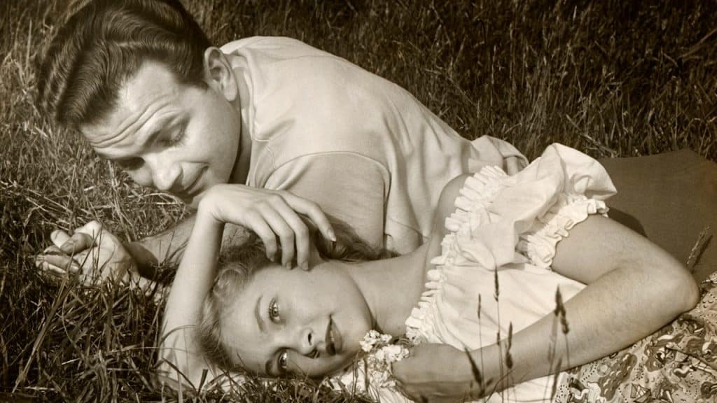 A romantic couple lying on grass outdoors.