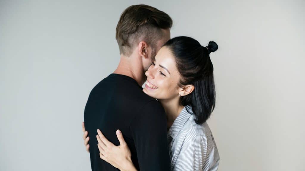 A woman with a joyful expression embraces a man against a plain white background.