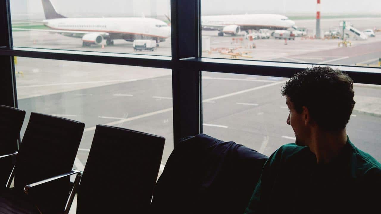 A man sitting in an airport terminal looking at planes outside.