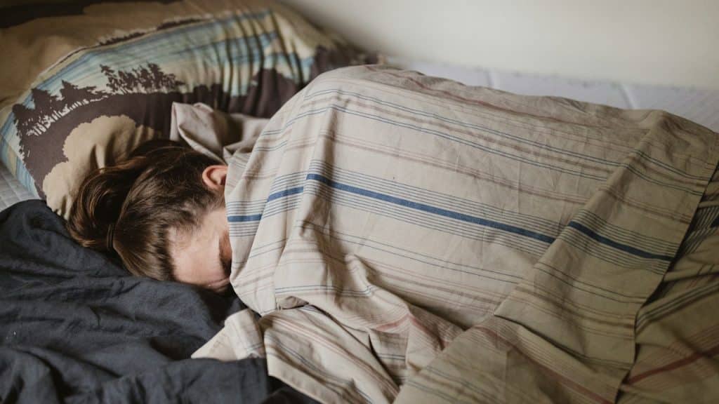 A person sleeping deeply, partially covered by a striped blanket.