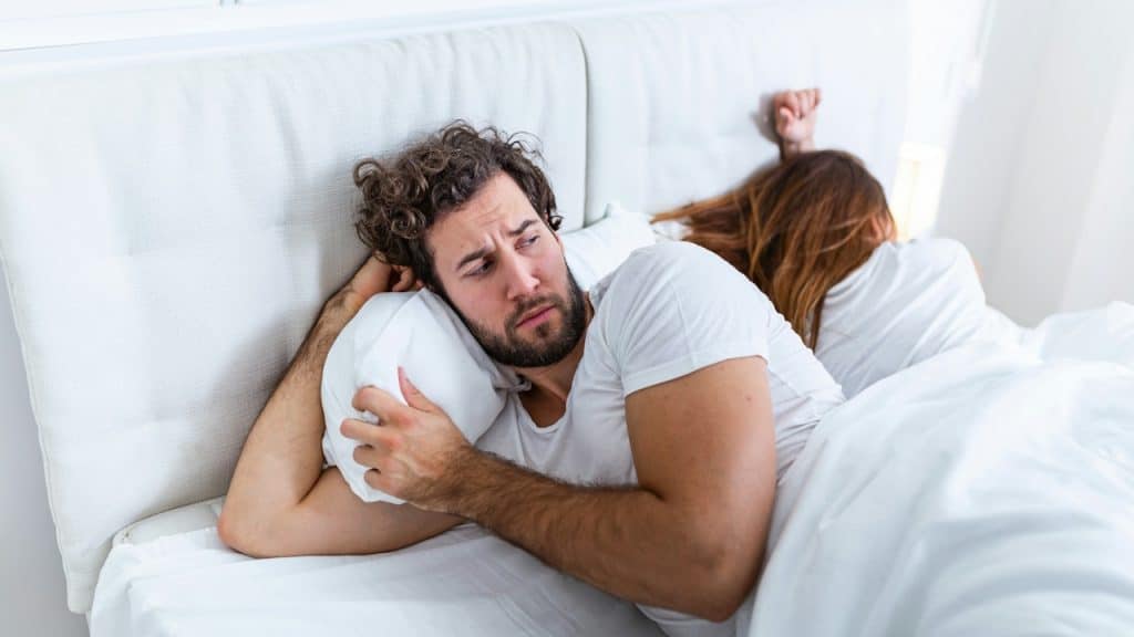 Man lying awake in bed next to a woman who is asleep.
