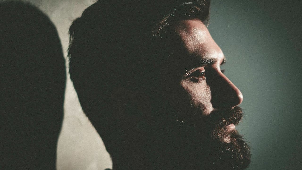 Close-up profile of a bearded man's face, partially illuminated by a side light.