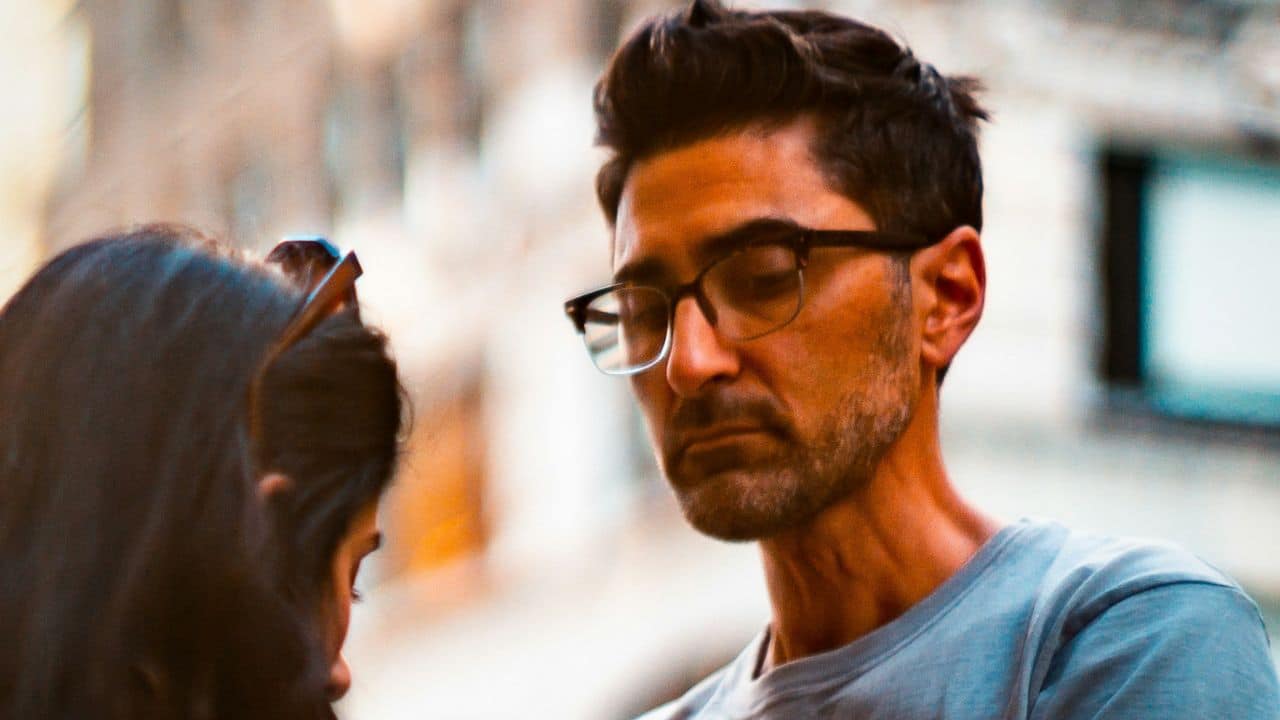 Close-up of a serious man in glasses looking down at a woman's dark hair.