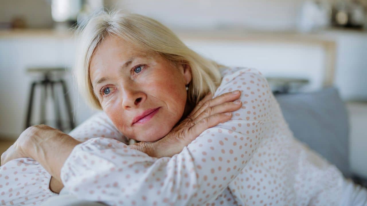 A blonde woman with her head resting on her arms looks pensively to the side.
