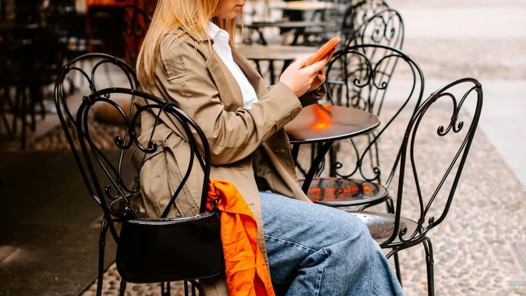 A woman sitting at an outdoor café looks at her tablet while holding it with both hands.