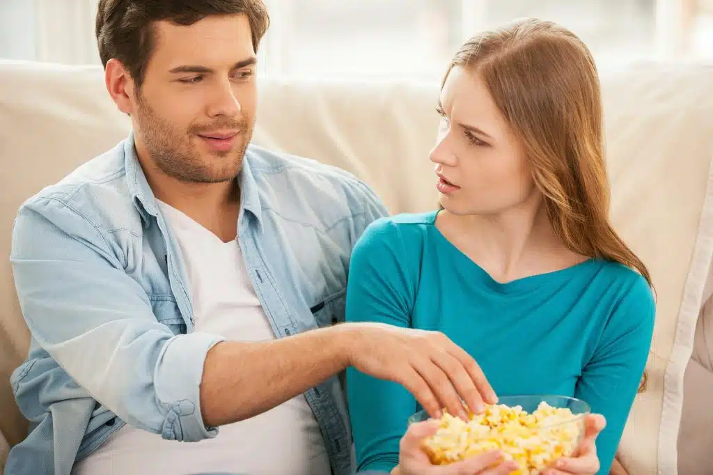 A woman is shocked when the man tries to get some of her snacks.