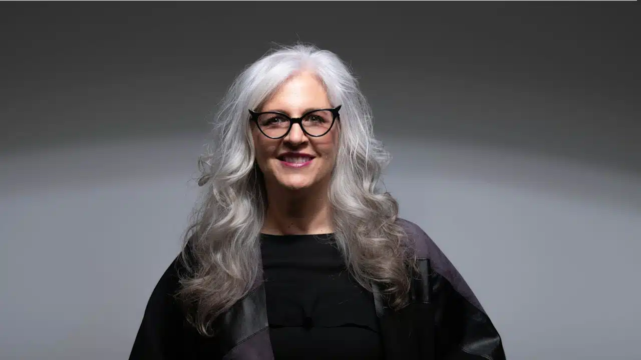 A man in a black dress wearing glasses is looking at the camera.