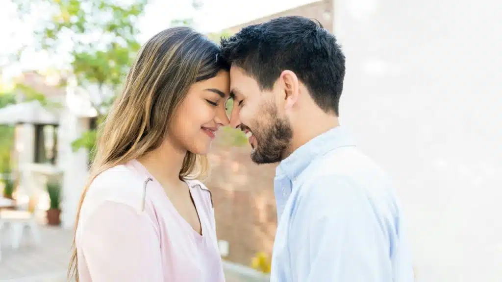 A smiling couple touching foreheads and standing close together in an outdoor setting.