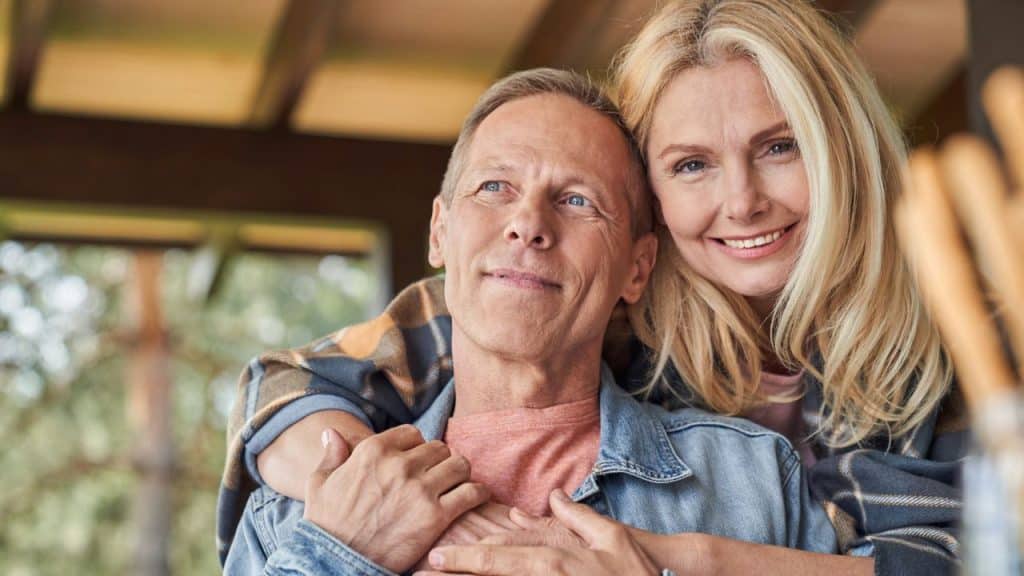 Middle-aged couple embracing and smiling outside, wearing casual denim and plaid shirts.