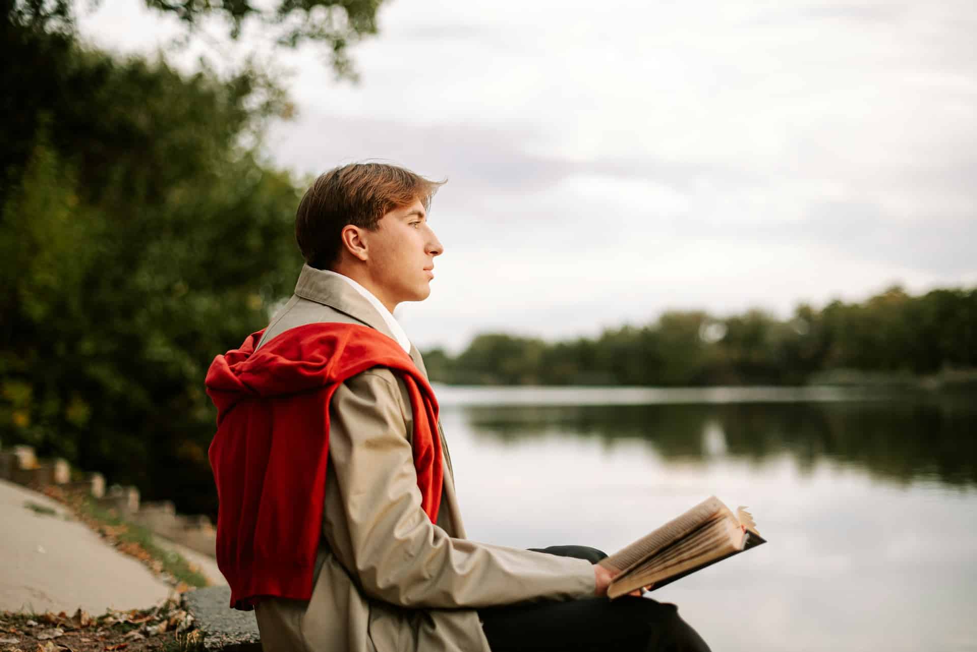 A man reading a book near a body of water. 