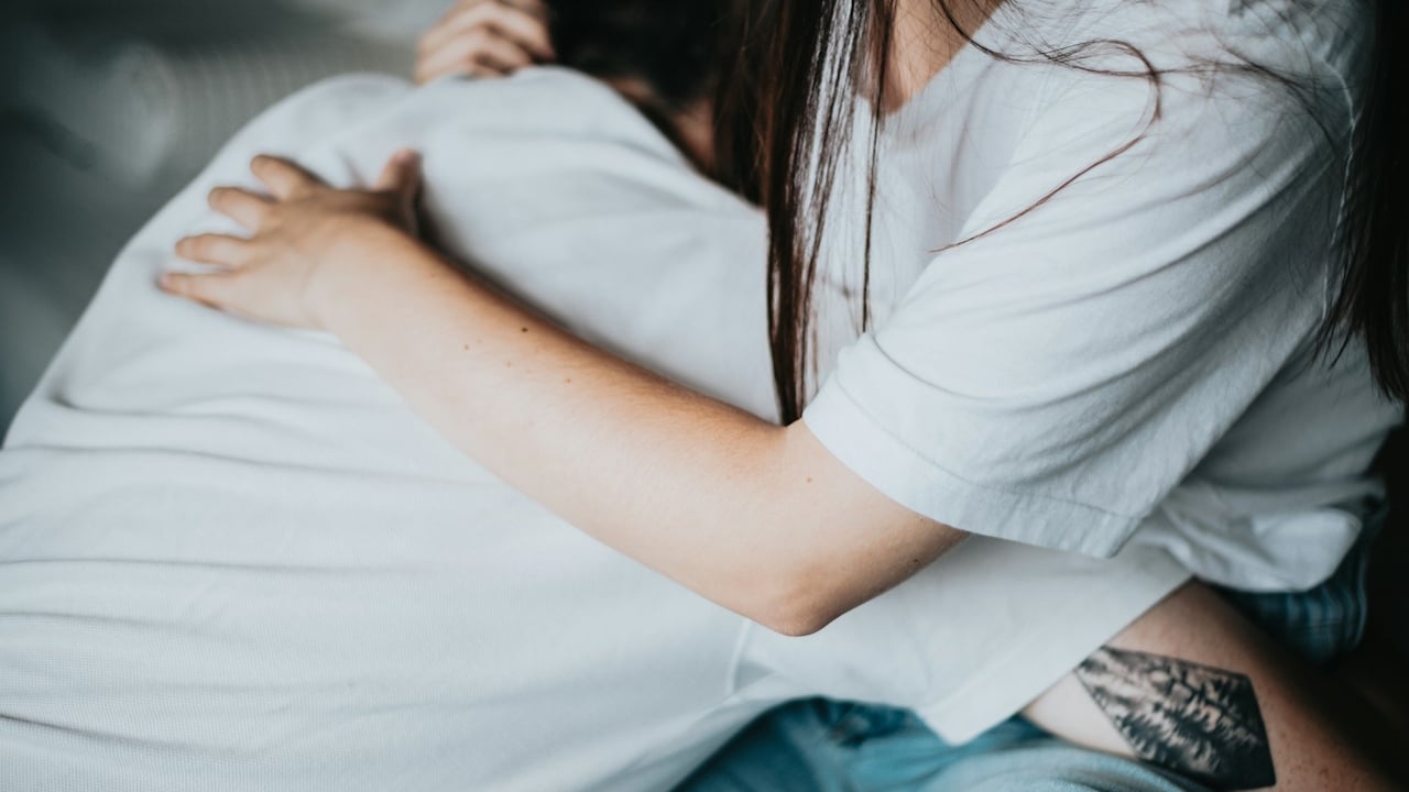 A close-up of a woman hugging a man tightly, with a visible tattoo on her thigh
