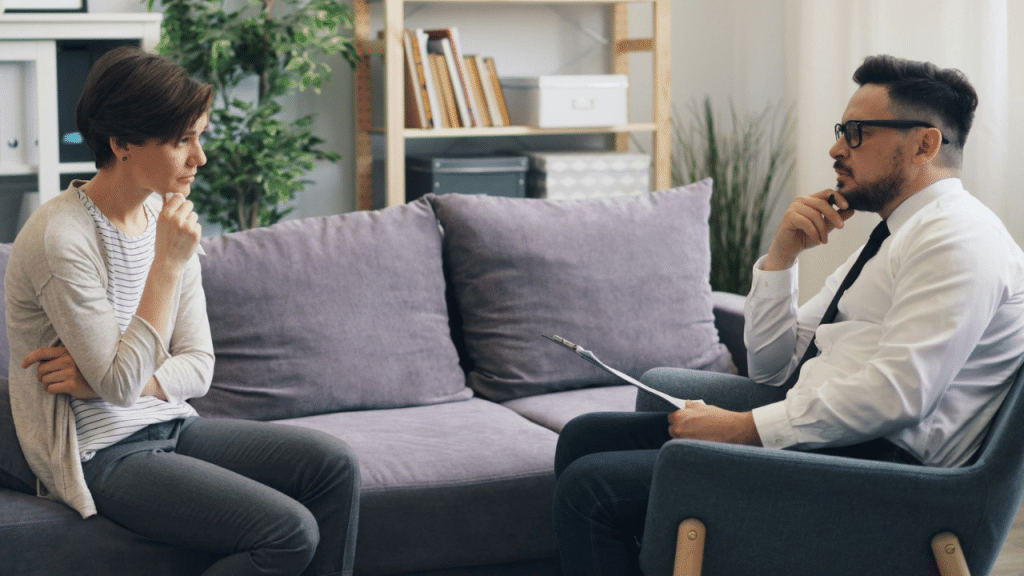 Woman and man in professional attire sitting across from each other on a couch and chair.