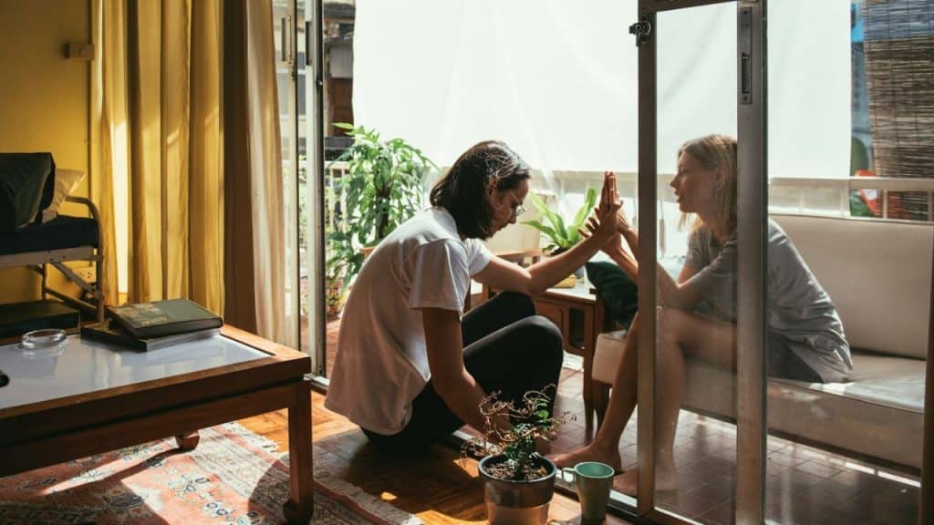 Two people touching hands through a glass door separating an indoor room and a balcony.