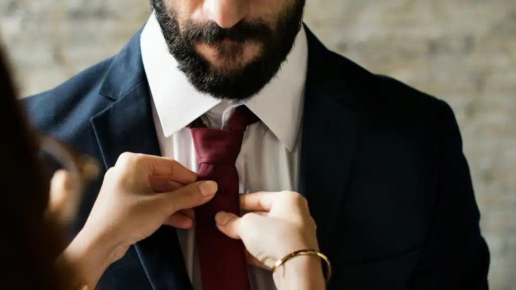 A person's hands adjust the red tie of a man wearing a dark suit.