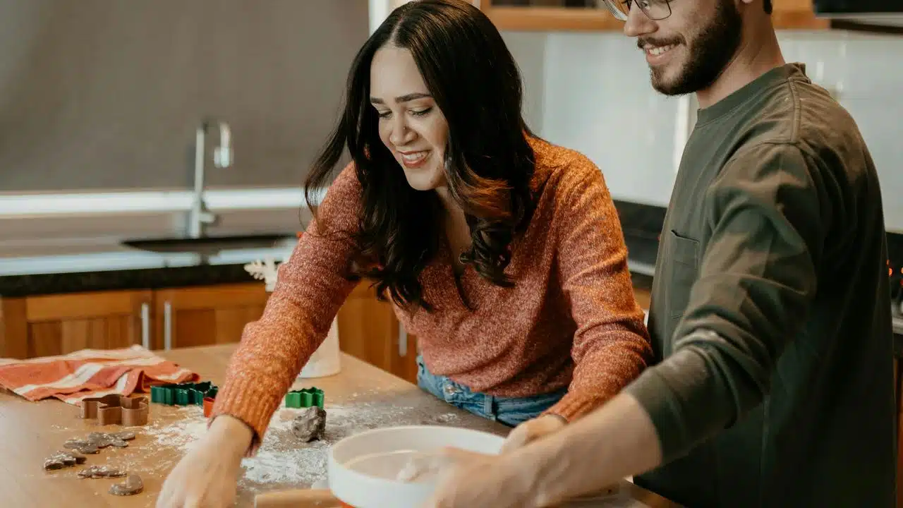 A smiling couple baking together in a kitchen.
