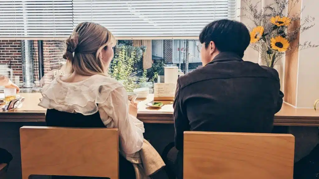 A blonde woman and a man sit side-by-side at a counter looking outside.