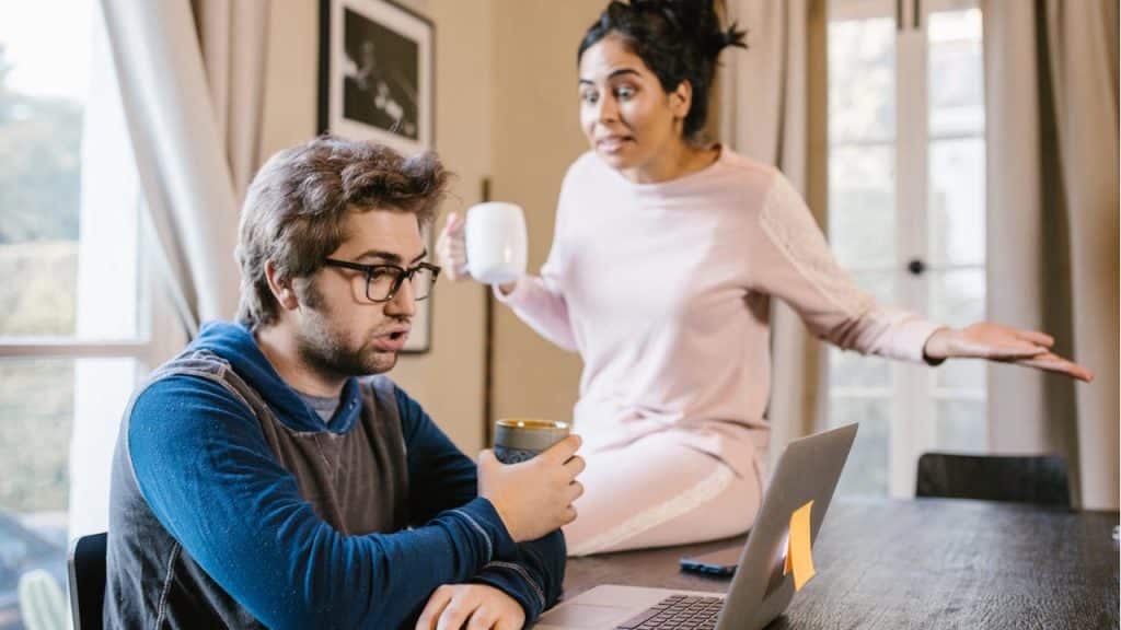 A man working on a laptop is interrupted by an angry woman holding a mug