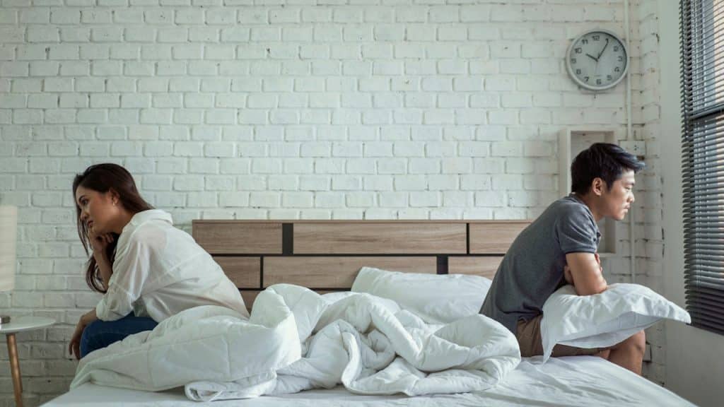 An unhappy couple sitting on the bed and not talking to each other.