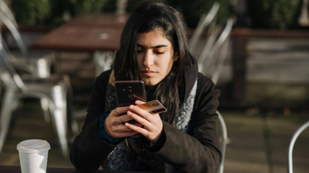 A woman checks her phone while holding a credit card.