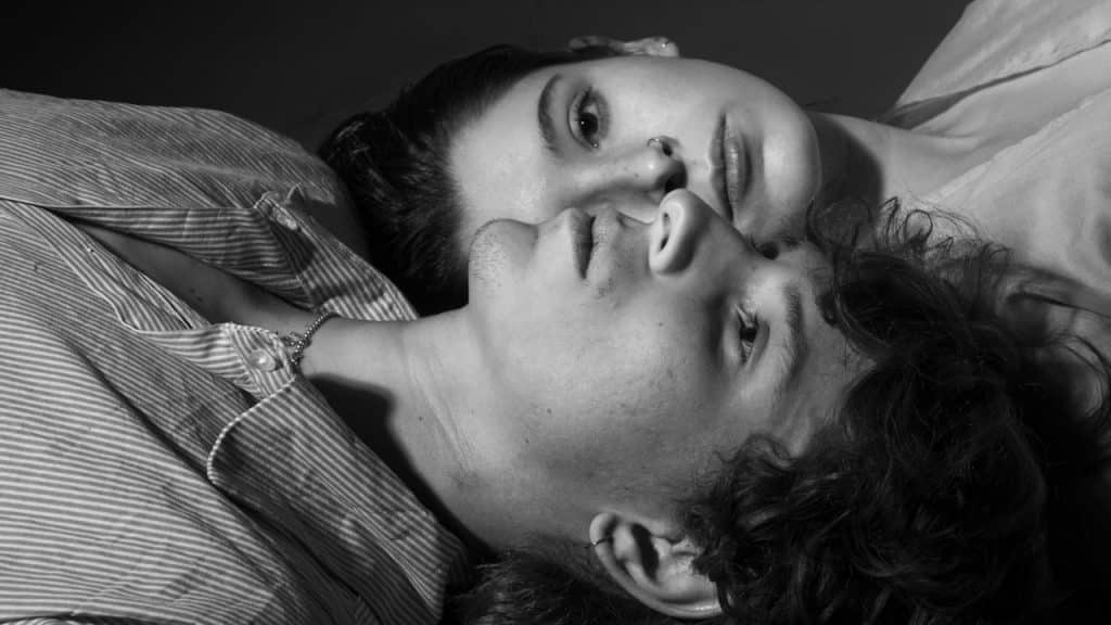A couple lying on the ground with their heads next to each other.