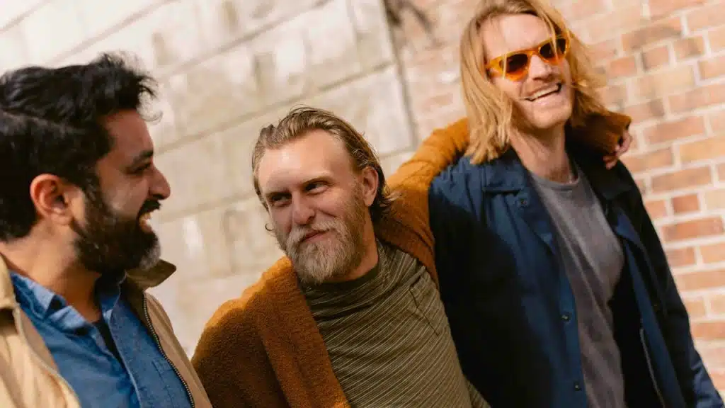 Three bearded men smiling and walking outside against a brick wall.