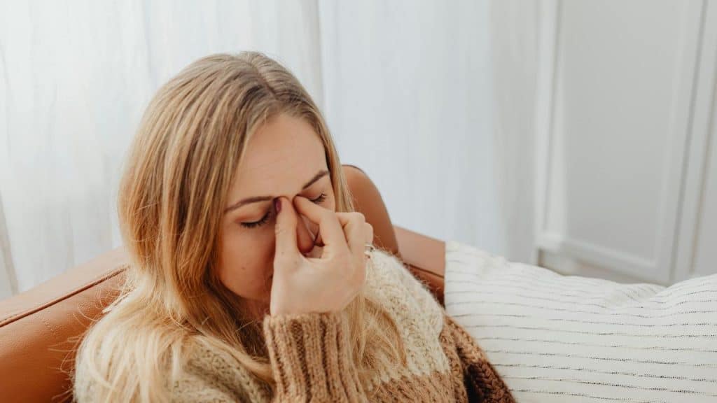 A woman sitting on a couch with her hand on her face, looking tired or stressed.