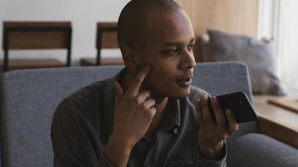 A person speaking into a smartphone while seated on a couch.