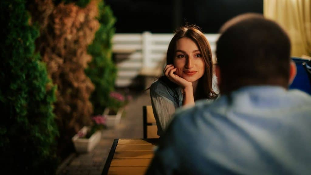 A woman with long dark hair rests her chin on her hand while looking at a man.