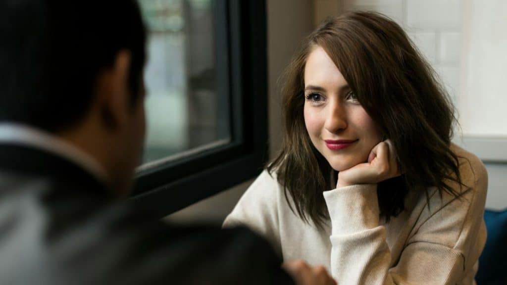 A woman with her chin resting on her hand smiles while looking at a man.