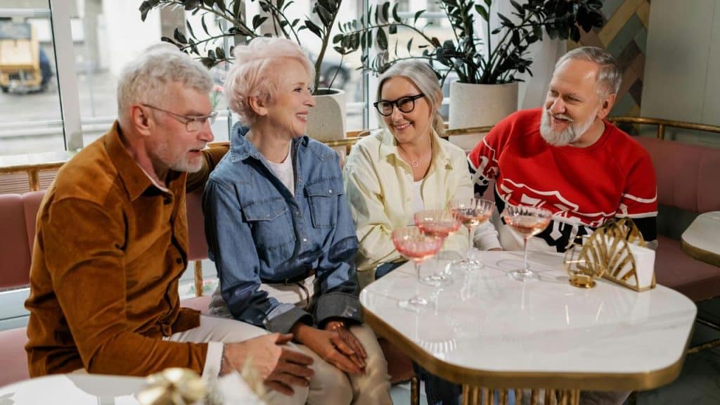 A group of four elderly friends sitting at a café table and chatting over drinks.