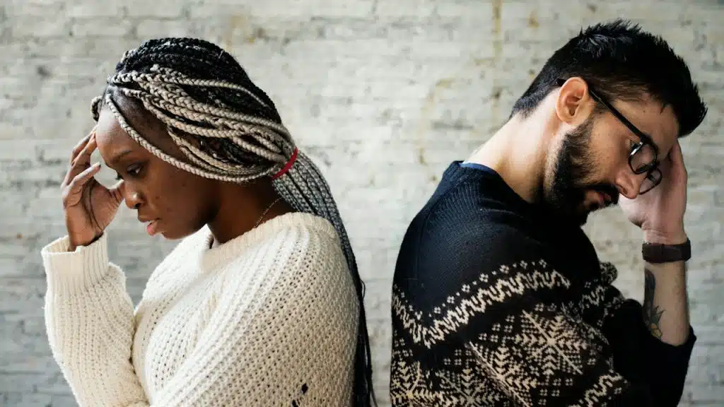 An upset couple holding their hands up to their heads and standing with their backs against each other.