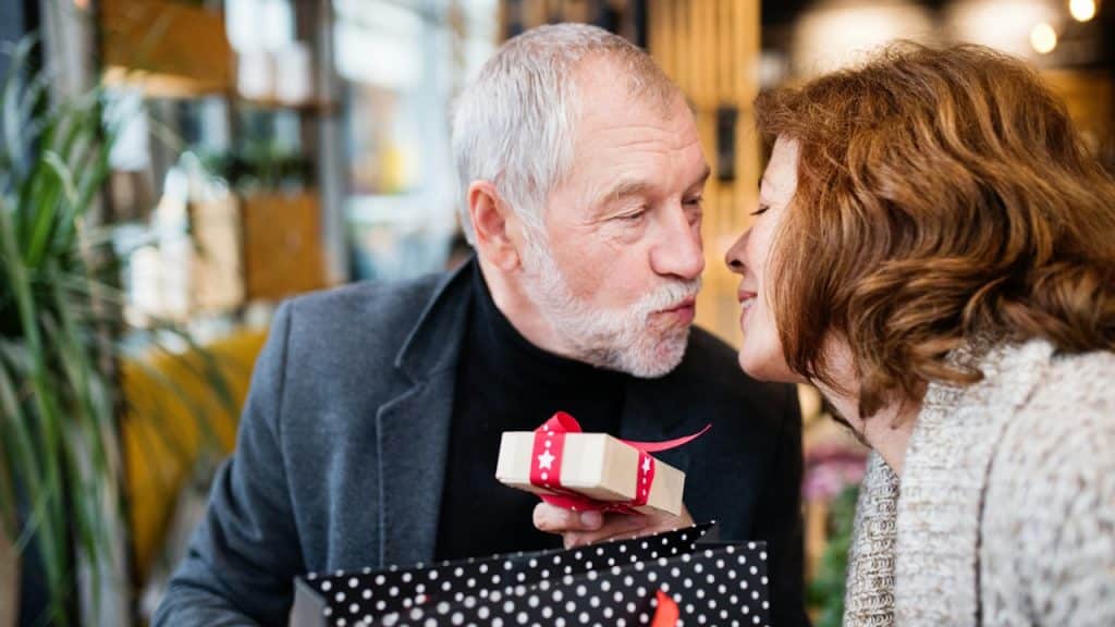 A man giving a present to a woman at a shopping center at Christmas time.