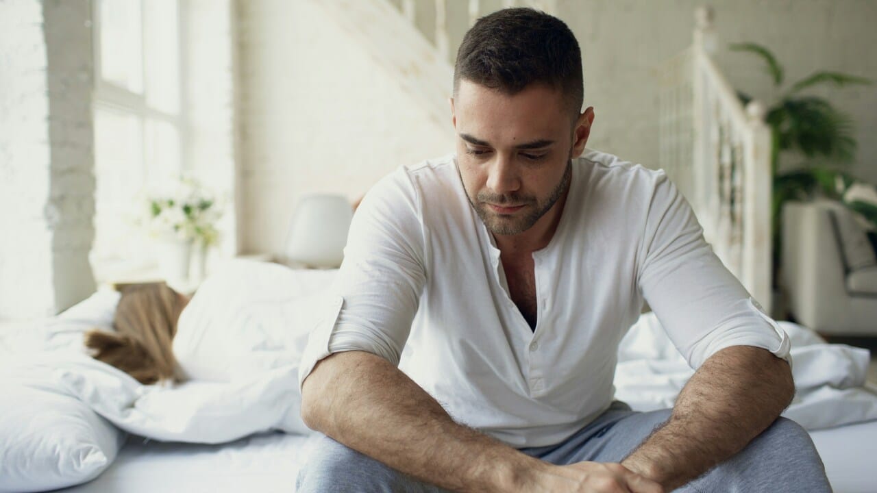 A man looking sad while his wife sleeps 