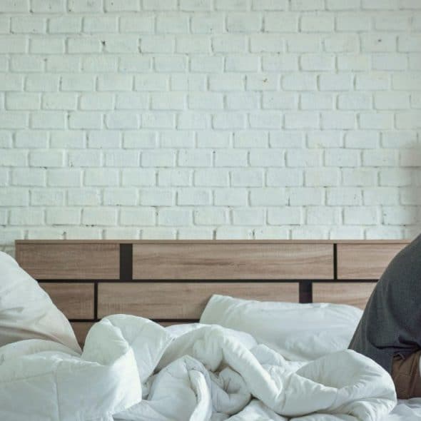 Man and woman sit turned away from each other on a bed with a white brick wall.