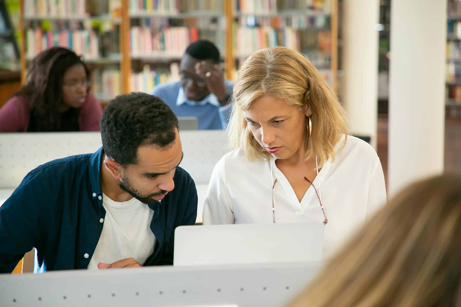 A man studying in the library with a professor.