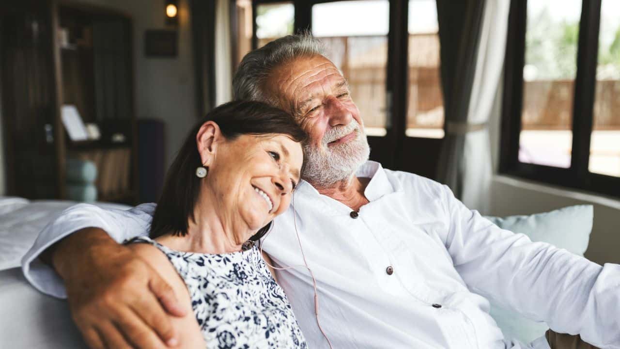 Smiling older couple relaxing together on a couch, with the woman leaning on the man's shoulder.