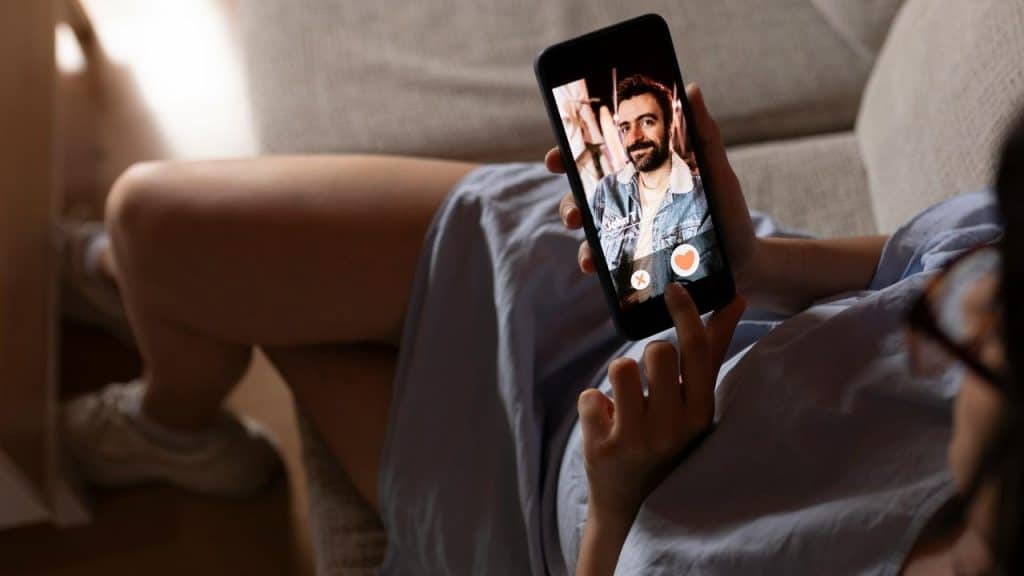 A person using a dating app on a smartphone while sitting on a couch.