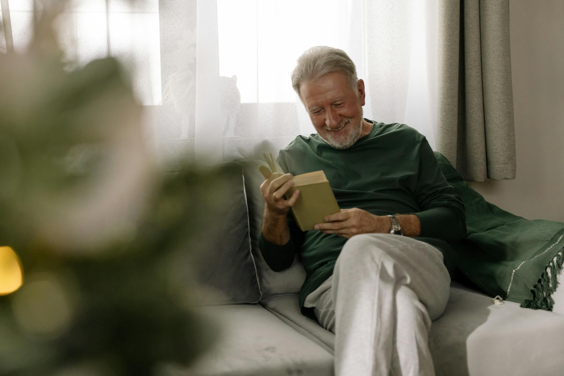 A smiling man in a green sweater sitting on the couch.