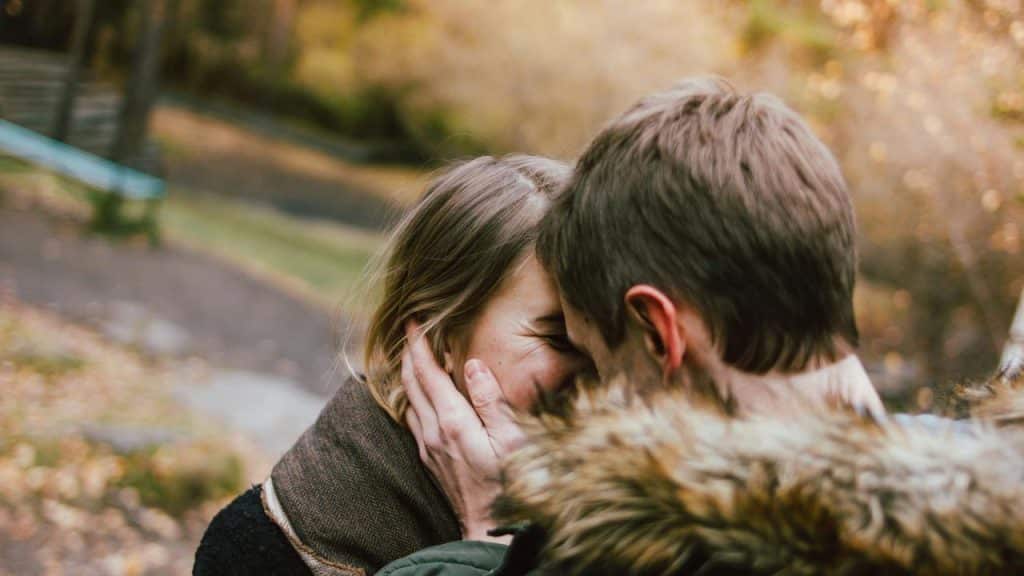 A couple shares a close moment outdoors in an autumn park.