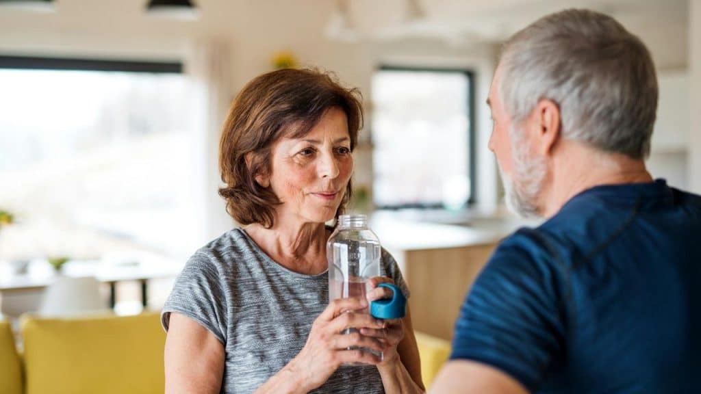 A woman drinking water from a bottle while her husband looks at her.
