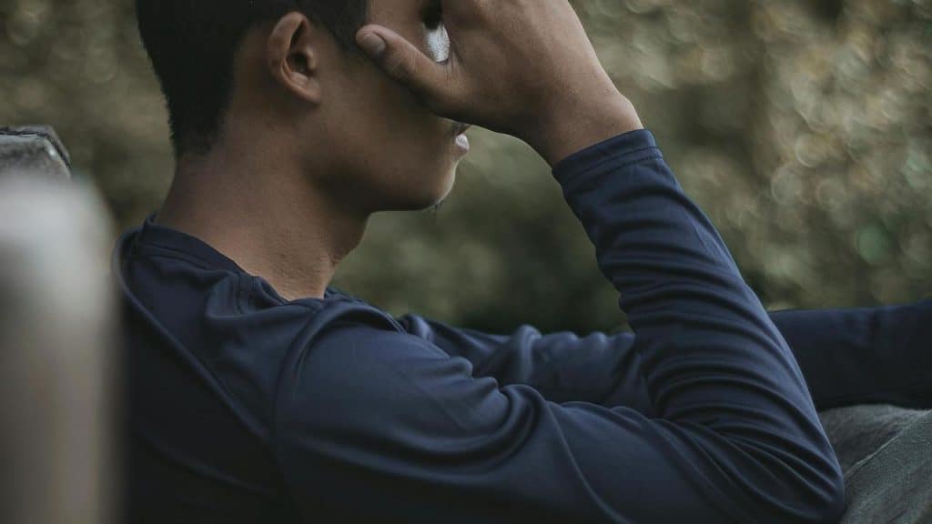 A person sitting outside with their hand covering part of their face.