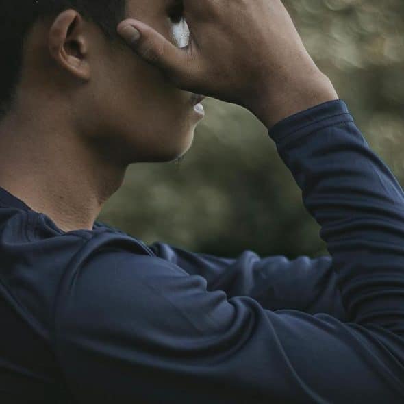 A person sitting outside with their hand covering part of their face.