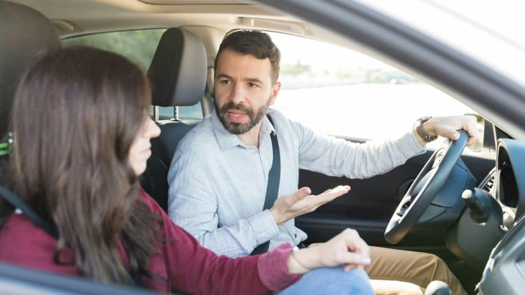 Man and woman in a car, the man is gesturing and talking to the woman.