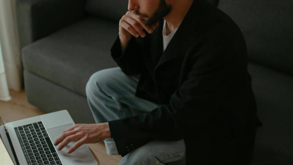 A person thoughtfully using a laptop while sitting on a couch.
