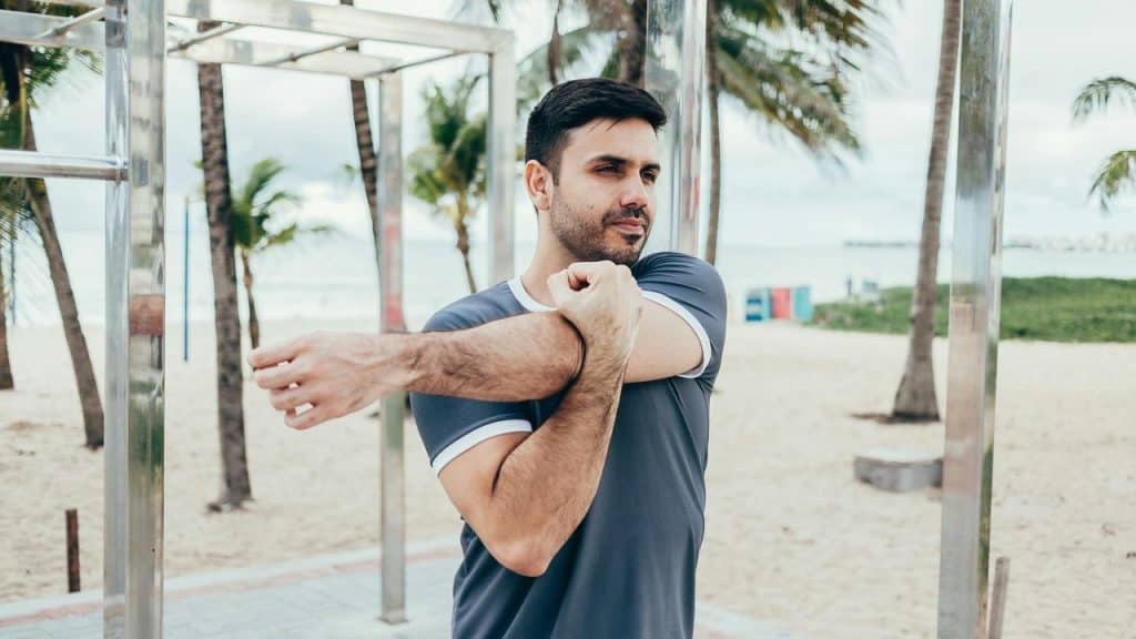 A person stretching their arm at an outdoor beach workout area.