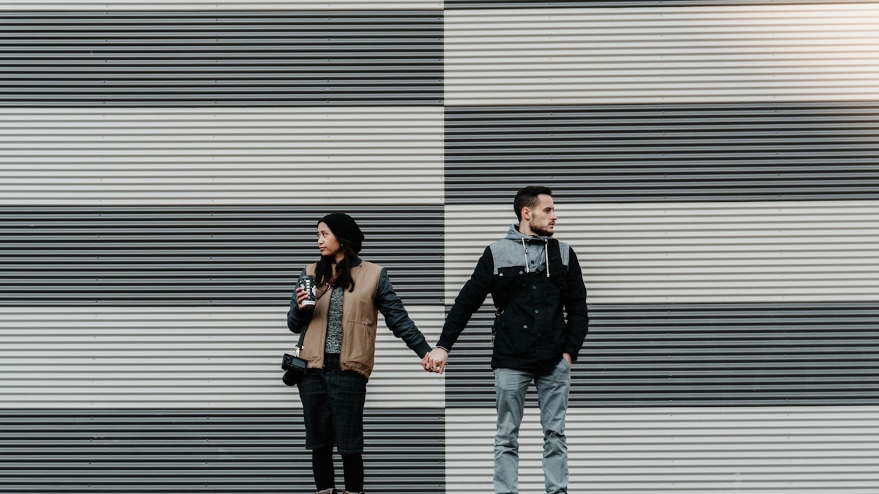 A couple holding hands and looking in opposite directions.