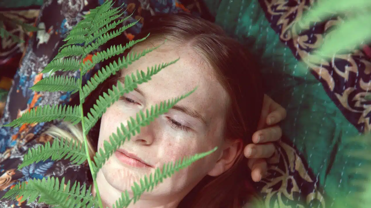 A woman in a white shirt is lying on green leaves.
