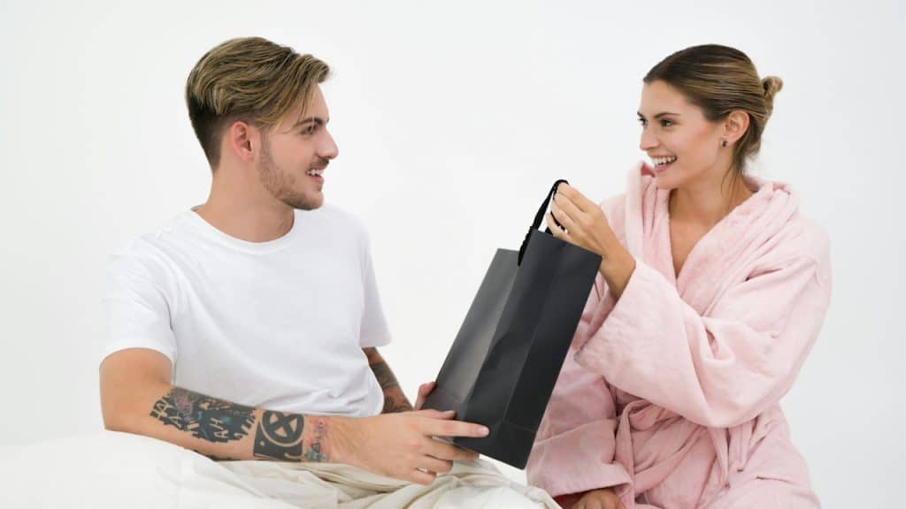 A woman holding a black paper bag sitting in front of the man.