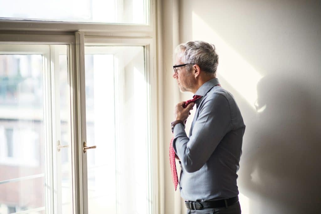 A man standing in a hotel room fixing his tie.